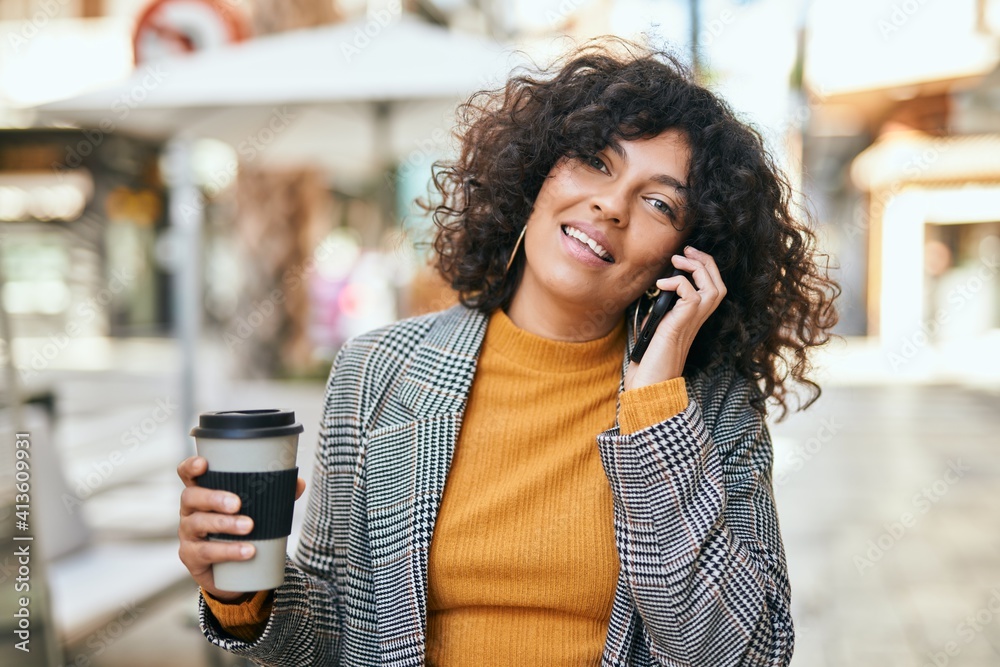 Young hispanic businesswoman talking on the smartphone drinking coffee at the city.