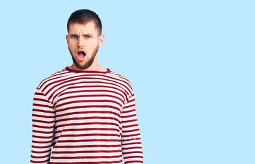 Young handsome man wearing striped sweater in shock face, looking skeptical and sarcastic, surprised with open mouth