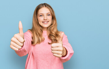 Beautiful young caucasian girl wearing casual winter sweater approving doing positive gesture with hand, thumbs up smiling and happy for success. winner gesture.