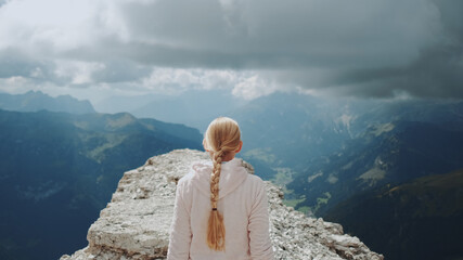 Back view of blonde woman walking on the top of the mountain under the clouds. Stunning view