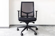 Modern black office chair in an empty office against white wall on gray carpet