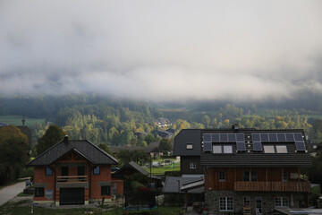 Canvas Print - Houses with black roofs and solar panels - dense trees under the thick clouds