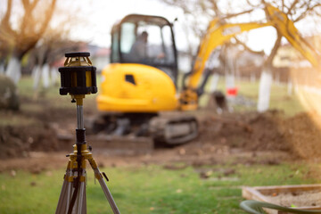 Wall Mural - Portrait of surveyor engineer using equipment with theodolite and total station and excavator doing landscaping works.