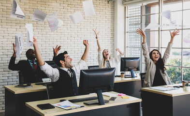 Group of four professional African and Caucasian businessmen and businesswomen celebrating their successful trendy project by throwing a document papers in the air with funny happy smiling