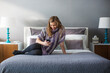 © Cavan Images - Woman using smart phone while sitting on bed at home