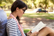© Cavan Images - Side view of woman reading book while sitting with man at park