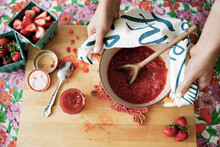 Overhead View Of Woman Holding Strawberry Preserve In Bowl On Cutting Board