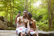 © Cavan Images - Woman kissing man taking selfie through smart phone on river bank in forest