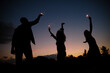 © Cavan Images - Silhouette of friends playing with sparklers against sky at night