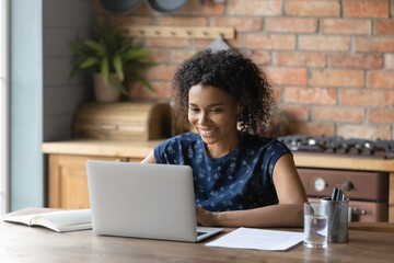 Close up smiling African American woman using laptop in kitchen, shopping or chatting online, watching webinar or movie, happy businesswoman, student working on research project, browsing apps