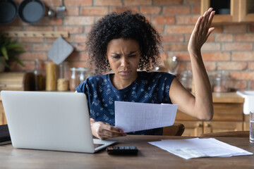 Wall Mural - Close up unhappy African American woman calculating bills, irritated by financial problem, unexpected debt, bankruptcy, holding document or receipt, lack of money, sitting at table with laptop