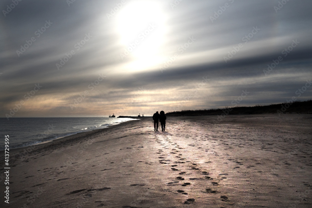 Szerokie ujęcie pod światło romantycznej pary spacerującej brzegiem morza - obrazy, fototapety, plakaty 