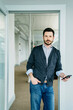 © Cavan Images - Portrait of businessman holding phone while standing at doorway in office
