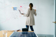 © Cavan Images - Rear view of businesswoman writing on whiteboard while working over solar panels in office