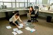 © Cavan Images - Businesswomen arranging documents on floor in office