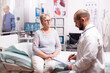 © DC Studio - Senior woman listening doctor talking about treatment in examination room. Elderly patient having a converstation with medical stuff in private clinic during consultation.