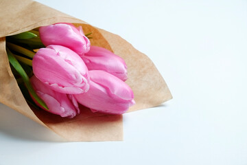 Wall Mural - A bouquet of pink french single late tulips in craft paper wrapping. Tender minimalistic spring flowers composition isolated on white background. Close up, copy space, top view, flat lay, studio shot.