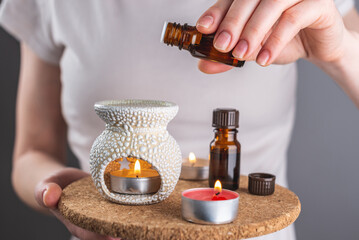 A woman is dripping organic essential oil into an aroma lamp for a relaxing and pleasant aromatherapy procedure. Closeup