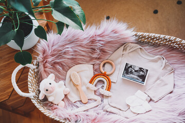 Baby changing basket with ultrasound image, baby bodysuit, soft and wooden toys. Still life of child products. Newborn background. Minimalist style photography of baby shower, pregnancy announcement.