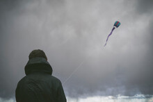 Rear View Of Hiker Flying Kite Against Storm Clouds