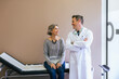 © Cavan Images - Smiling patient looking at doctor while sitting on bed against wall at hospital