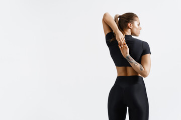 Wall Mural - Rear view of healthy and fit sports woman stretching arms before exercising, looking away determined. Sportswoman doing warm up workout on white isolated background