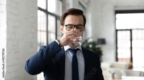Thirsty Caucasian man feel dehydrated hold glass drink clean mineral still water. Young businessman enjoy clear aqua for body balance or refreshment. Healthy lifestyle, hydration concept.