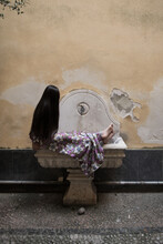 Girl In Dress Sitting On Old Fountain In Wall In Italy