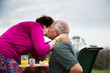 © Cavan Images - Side view of senior man kissing wife while at table against sky