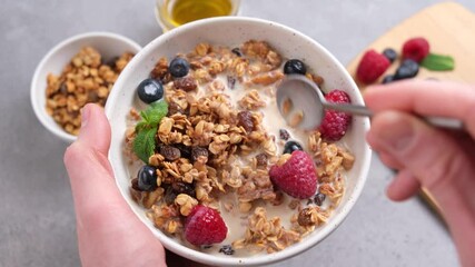 Wall Mural - Eating granola with raisins and berries. Healthy breakfast bowl in hands. Clean eating, dieting concept
