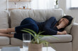 © fizkes - Depressed frustrated young asian woman lie on couch alone cry feel bad have health love problem. Stressed upset teenage female snuggle down on sofa suffer of pain grief loneliness think that life ends