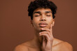 © Ivan - Photo of attractive black man with piercing touches his smooth face with eyes closed. Naked torso, isolated brown color background