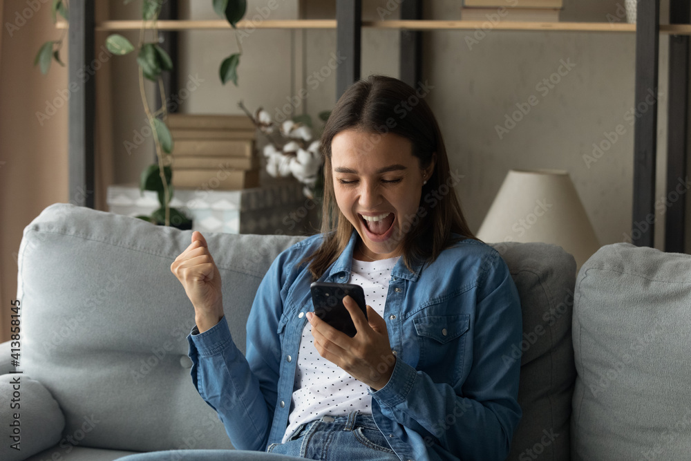 Amazed millennial female student hold smartphone yell in delight motivated with new opportunities reading perfect job offer. Happy young woman feel lucky celebrate receiving unexpected lottery prize - obrazy, fototapety, plakaty 