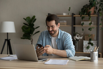 confident man sitting at desk taking break in work with electronic documents on laptop to make answe
