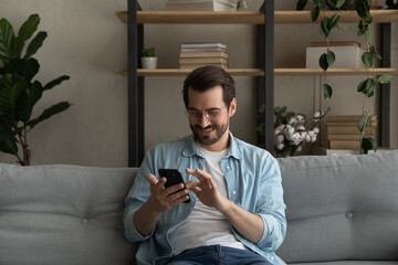 Wall Mural - content young man relax on sofa use smartphone spend free time online in social network chat at web 