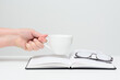On the open diary are glasses . A woman holds a white cup in her hand. Concept-business, education