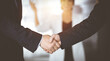 © cameravit - Unknown businesspeople are shaking their hands after signing a contract, while standing together in a sunny modern office, close-up. Business communication, handshake, and marketing concept