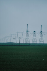 Poster - Vertical shot of high-voltage transmission towers under a rainy cloudscape