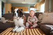 © Cavan Images - Portrait of cute baby boy sitting with dog on couch in living room at home
