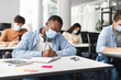 © Prostock-studio - Black male student in mask sitting at desk and writing
