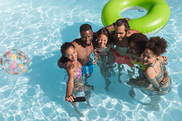 Diverse group of friends having fun and taking selfie in swimming pool