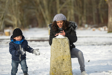 Wall Mural - young boy playing with his mother under the snow during winter holidays