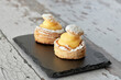 Appetizing puff pastry cakes filled with pastry cream on a black plate.