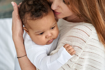 Wall Mural - Loving young caucasian mother hugging cute infant african american baby daughter expressing single parent love, tenderness and care. Diverse mum and adorable ethnic little child girl bonding.