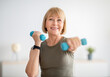 © Prostock-studio - Home training concept. Strong senior woman doing exercises with dumbbells indoors