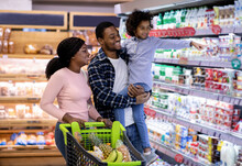Family Shopping Concept. African American Parents With Lovely Daughter Buying Food At Supermarket