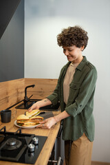 Wall Mural - Happy young brunette female in casualwear putting homemade sandwiches on plate