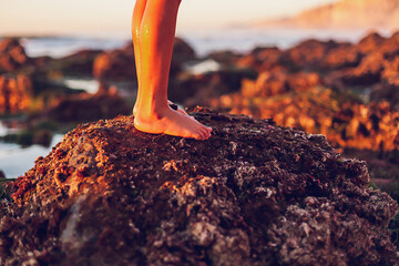 Wall Mural - Boy standing on a rock at the beach at low tide, focus on feet.