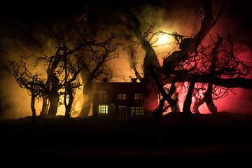 Old house with a Ghost in the forest at night or Abandoned Haunted Horror House in fog. Old mystic building in dead tree forest. Trees at night with moon. Surreal lights. Horror Halloween concept