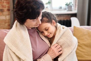 Poster - Affectionate cute little girl embracing her grandmother while resting on couch